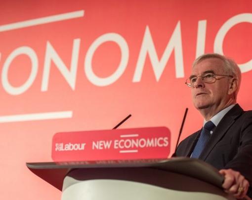 John McDonnell at a podium in front of the word "Economics" on a red background.