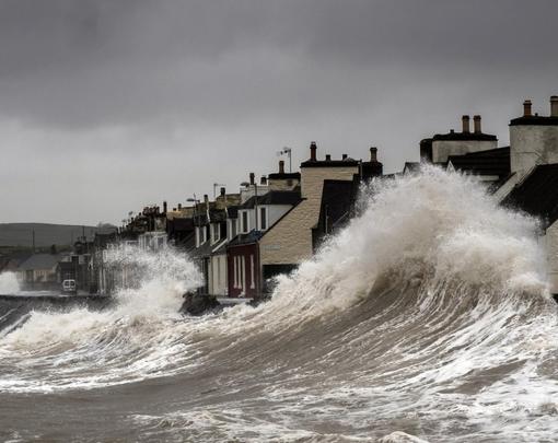 A storm surge pushing waves onto shore, threatening a row of houses.