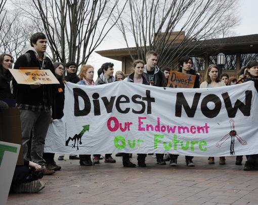 Students standing behind a banner that reads "Divest Now"