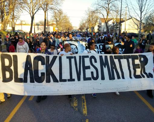 A group of protestors marching behind a banner that reads "Black Lives Matter"