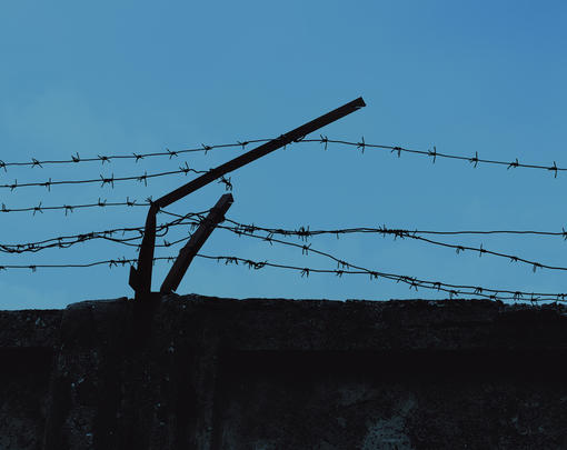 Strands of barbed wire on top of a wall, beginning to come apart.