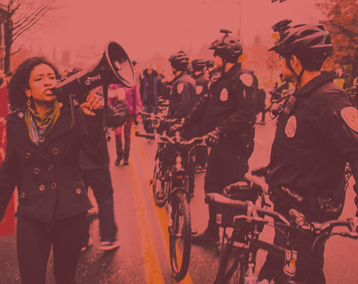 A women with a megaphone protests near a line of bicycle cops.
