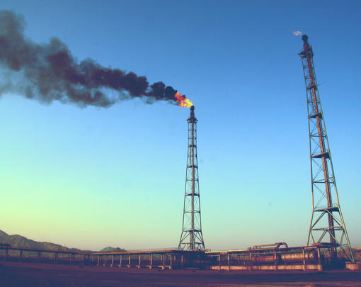 Two oil wells, one belching smoke and fire.