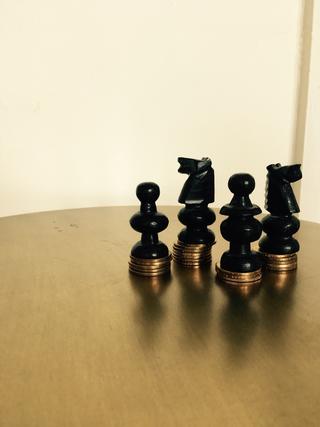 Various non-royalty chess pieces standing on roughly equal piles of coins