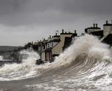 A storm surge pushing waves onto shore, threatening a row of houses.
