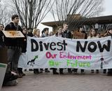 Students standing behind a banner that reads "Divest Now"