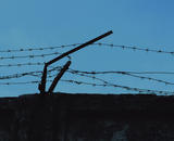 Strands of barbed wire on top of a wall, beginning to come apart.