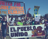 Signs carried by marchers reading "El Pueblo Unido" and "United for Jobs Justice and Climate"