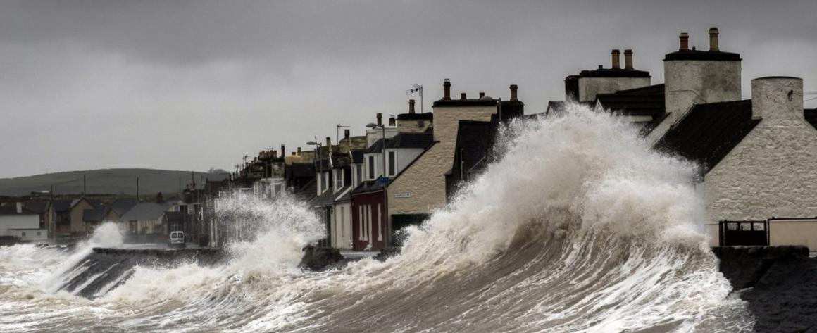 A storm surge pushing waves onto shore, threatening a row of houses.