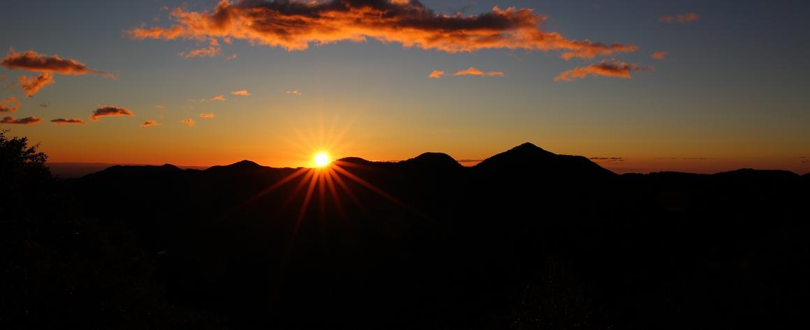 A sun about to either rise or set behind a mountain range.