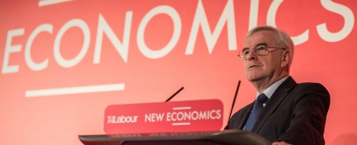 John McDonnell at a podium in front of the word "Economics" on a red background.
