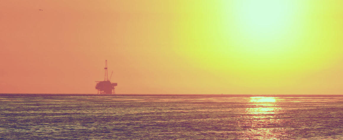 The sun setting with an ocean-based oil rig on the horizon
